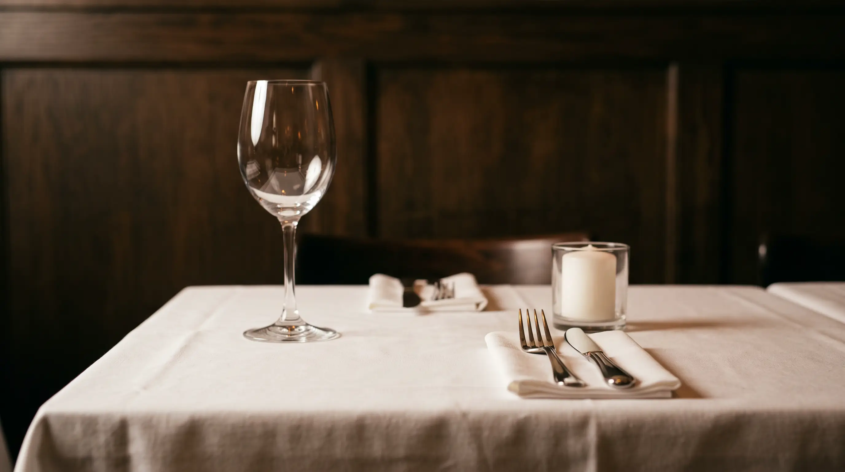 Table dressée de restaurant : nappe blanche, verre à vin vide, couverts et bougie