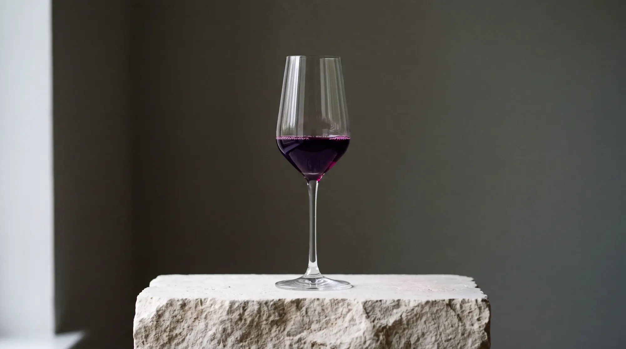 Verre de dégustation contenant un vin rouge profond, posé sur une pierre calcaire