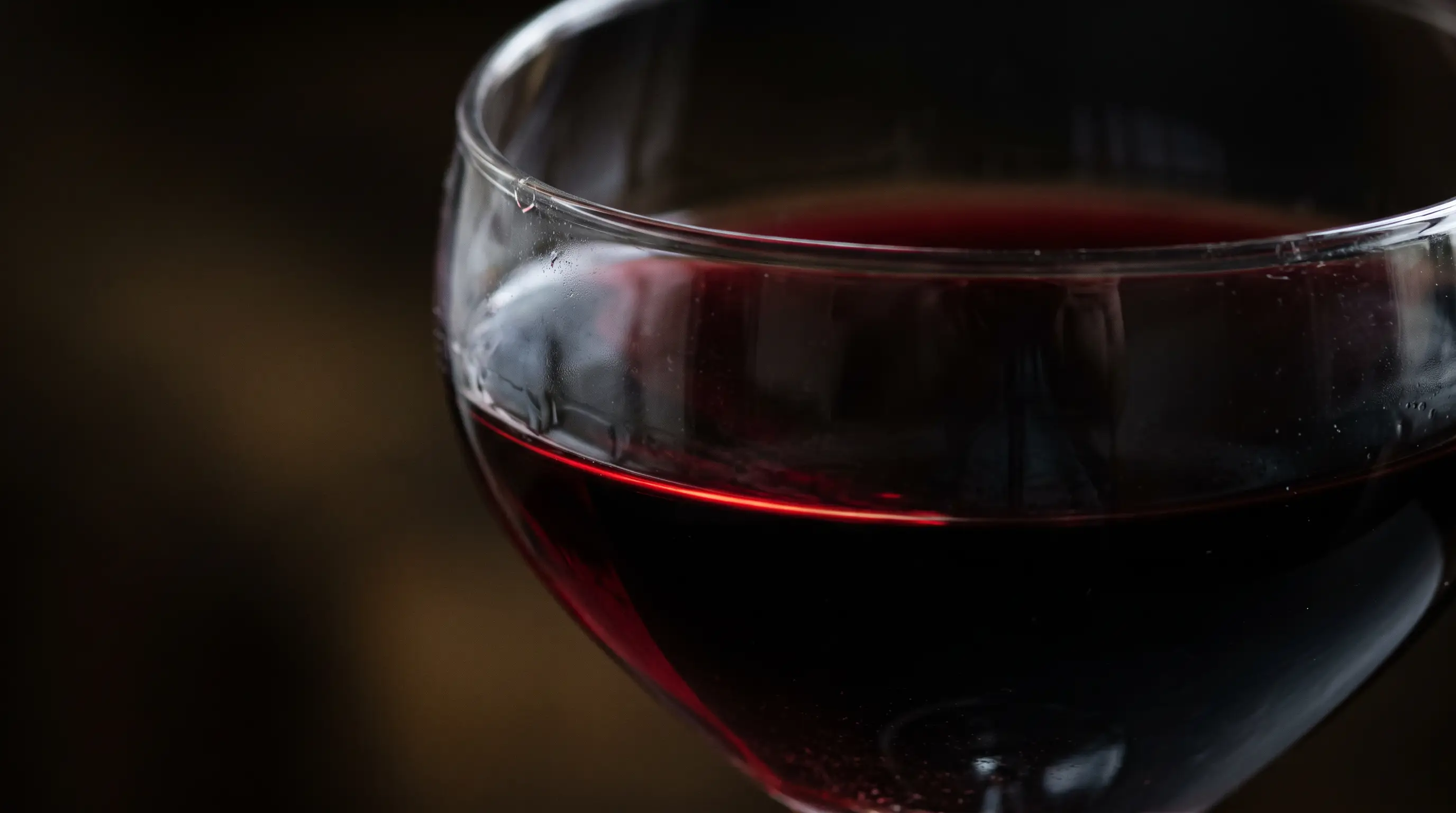 Macro d’un vin rouge très sombre dans un verre, reflets grenat sur le ménisque